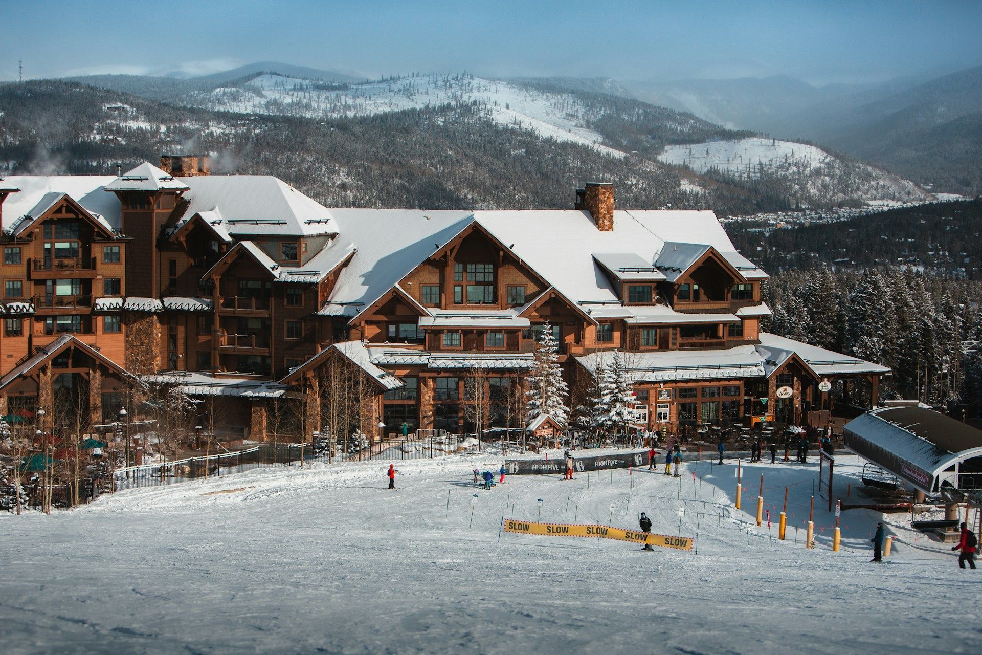 A large building with snow on the roof is surrounded by snow covered mountains.