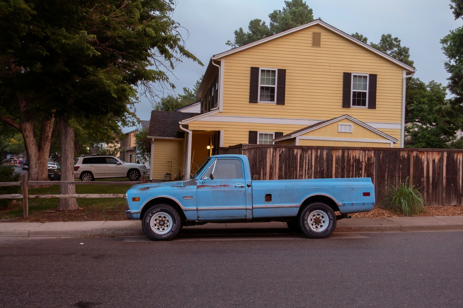 A blue truck is parked in front of a yellow house