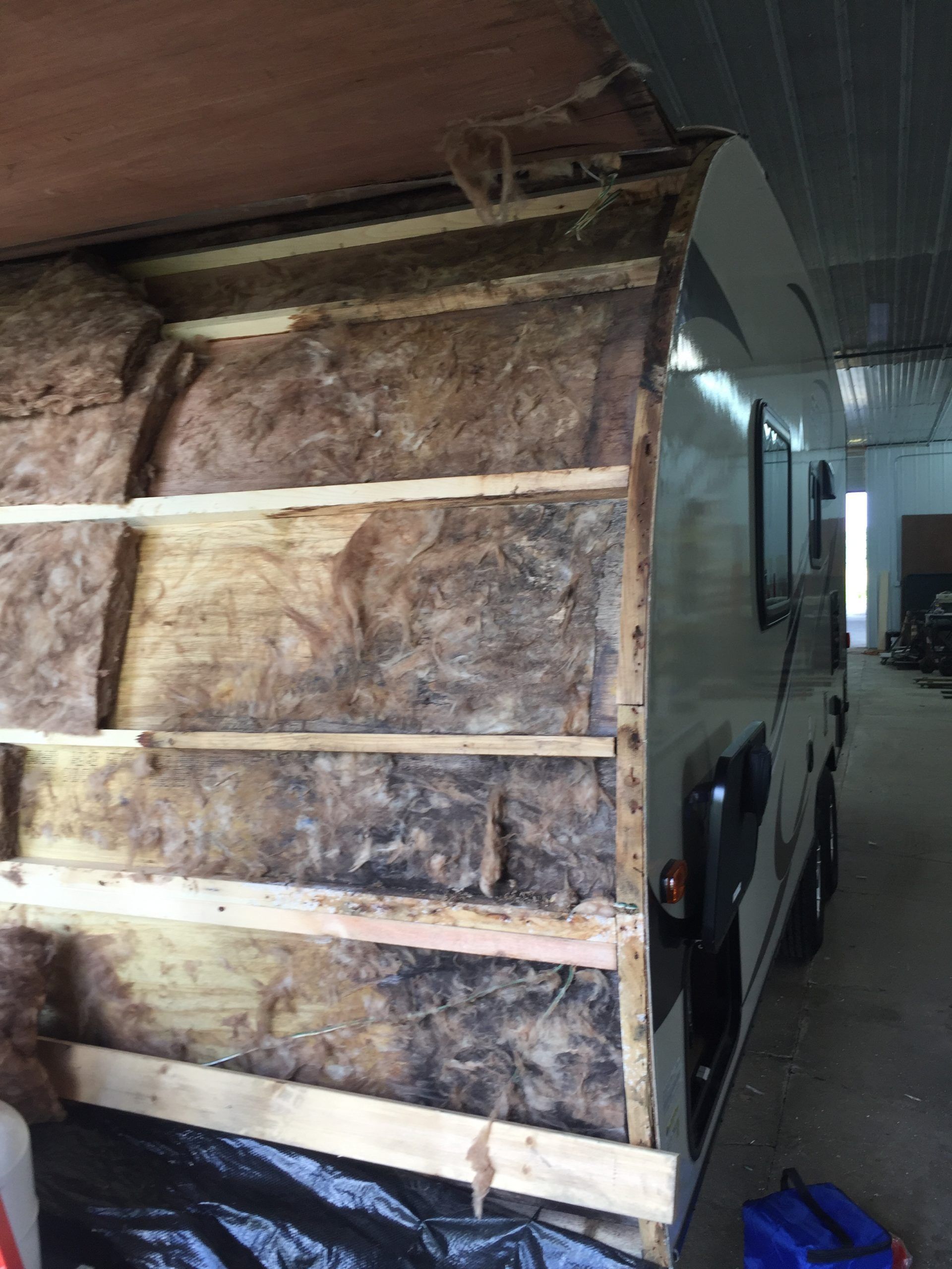 RV side partially disassembled, showing insulation and wood frame, next to intact exterior.