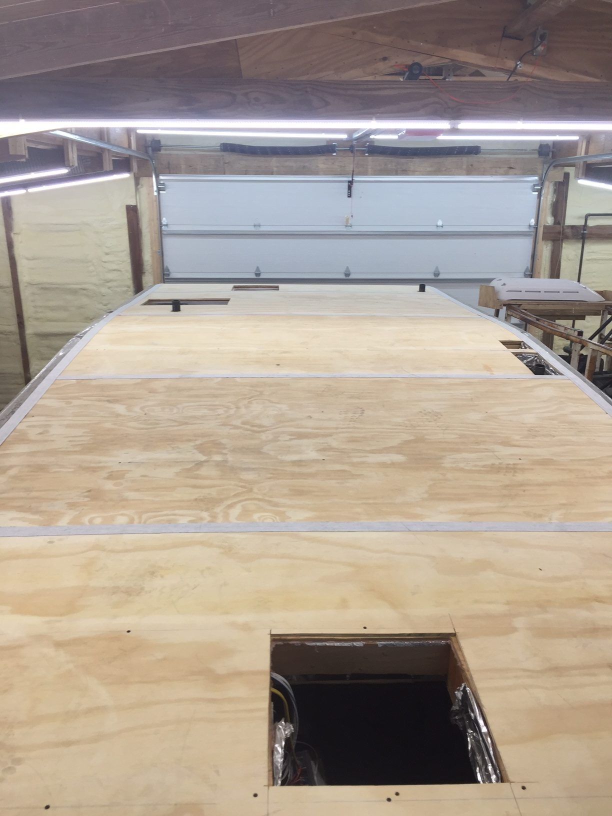 Wooden RV roof with cutouts for vents or access, inside a workshop with a closed garage door.
