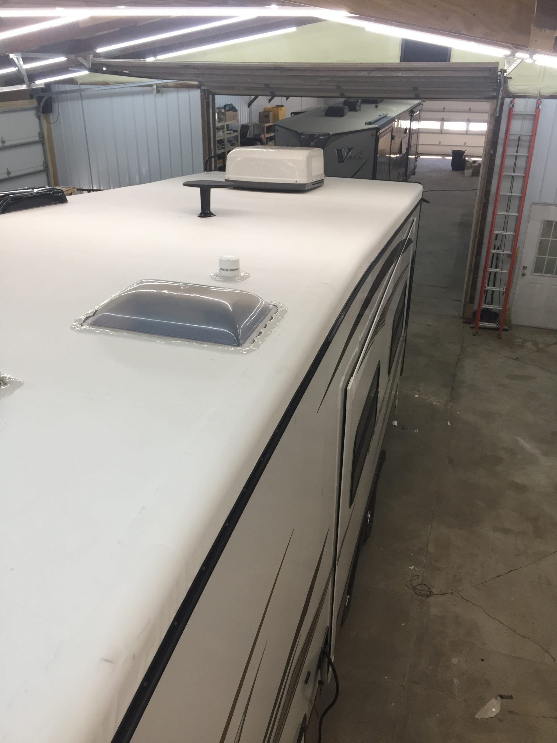 RV roof with white coating, air conditioning unit, and antenna inside a garage.