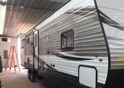 Gray and white travel trailer parked inside a building. Ladder is visible to the left.