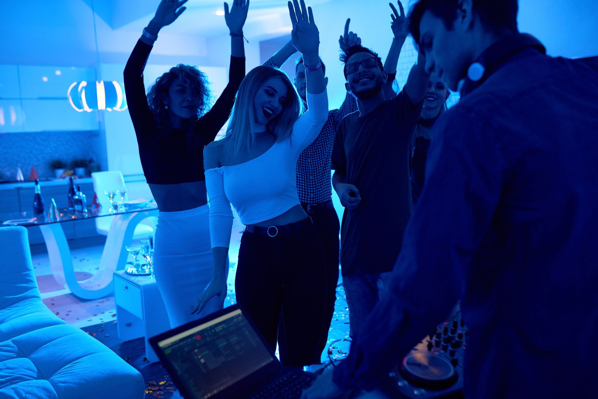 A group of people are dancing at a party while a dj plays music.