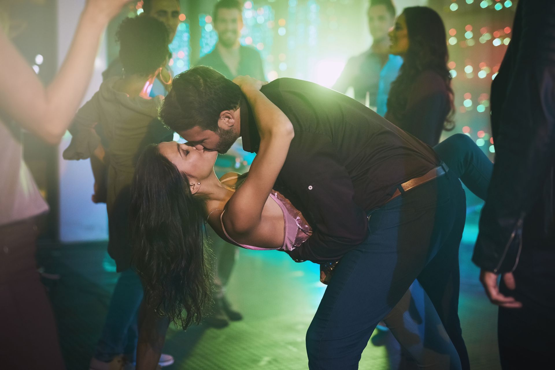 A man and a woman are kissing on a dance floor at a party.