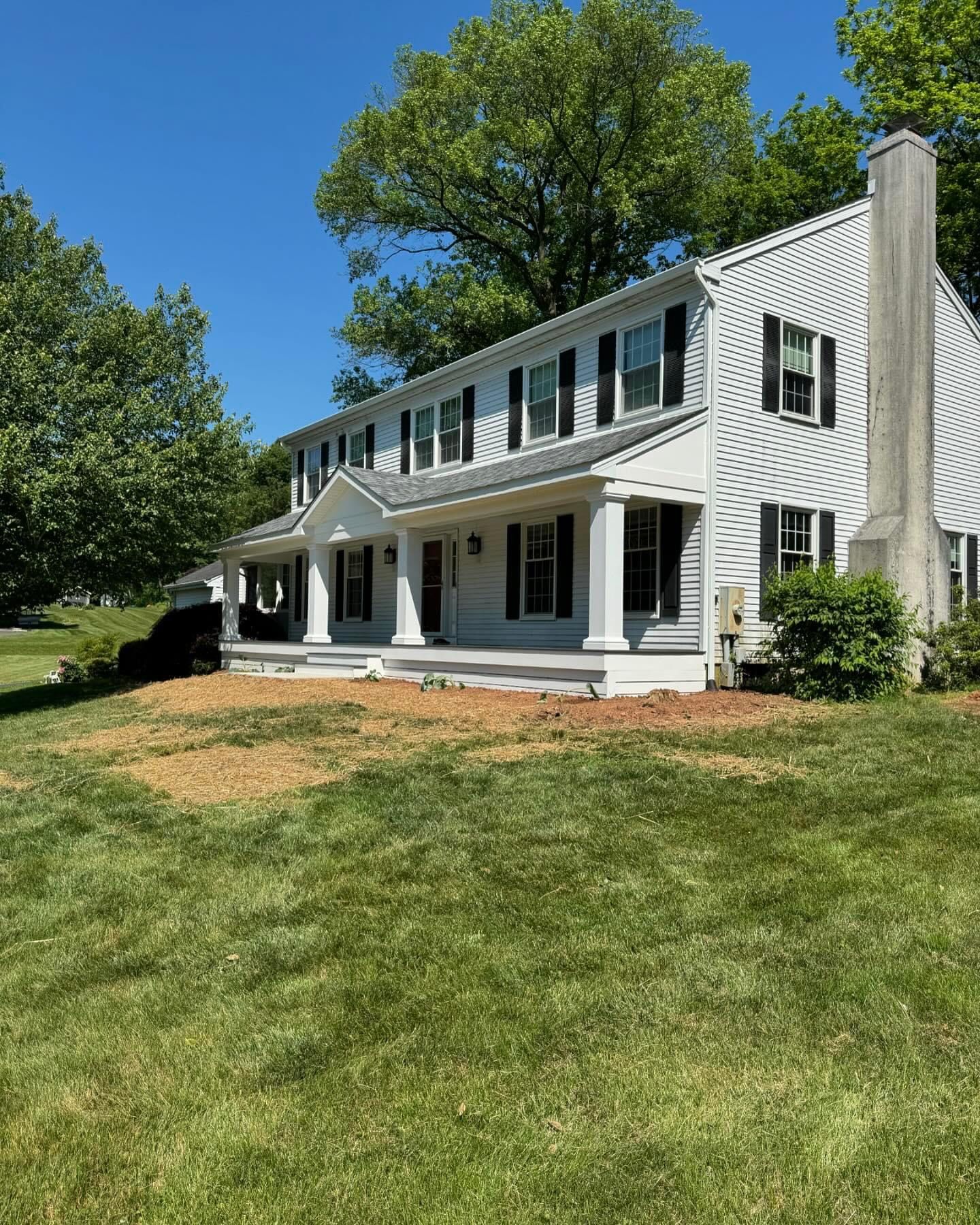 A large white house with black shutters is sitting on top of a lush green lawn.
