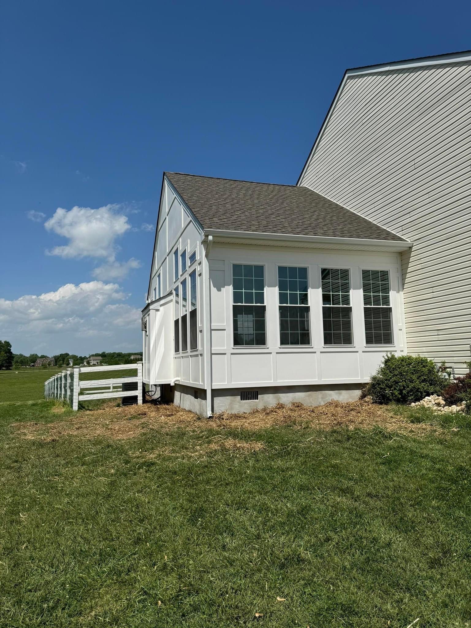 A white house with a porch and a fence in a grassy field.