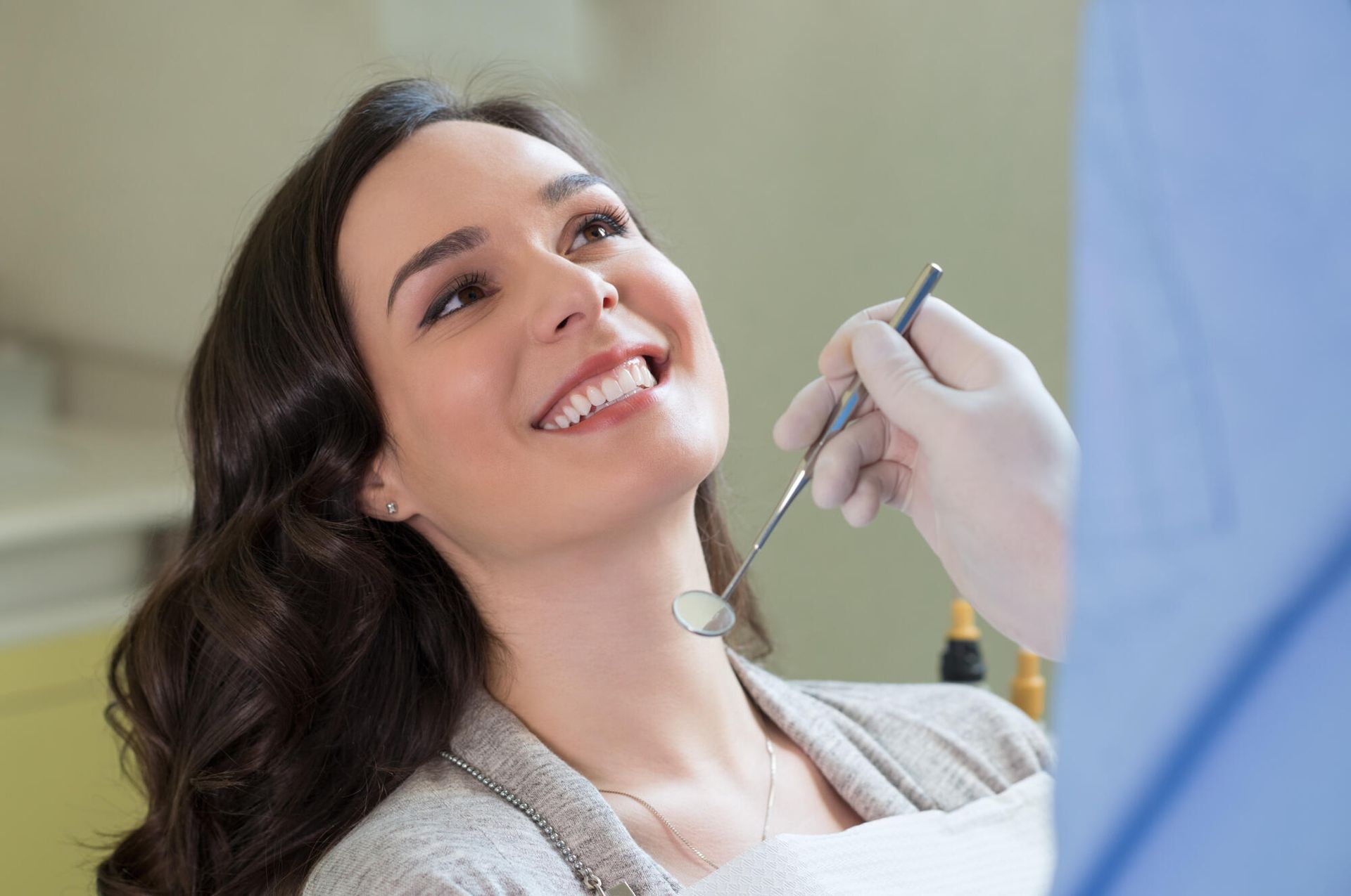 A smiling person in a dental chair looking at a dentist who is holding a dental mirror.