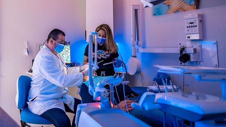 A dentist and a nurse are working on a patient in a dental office.