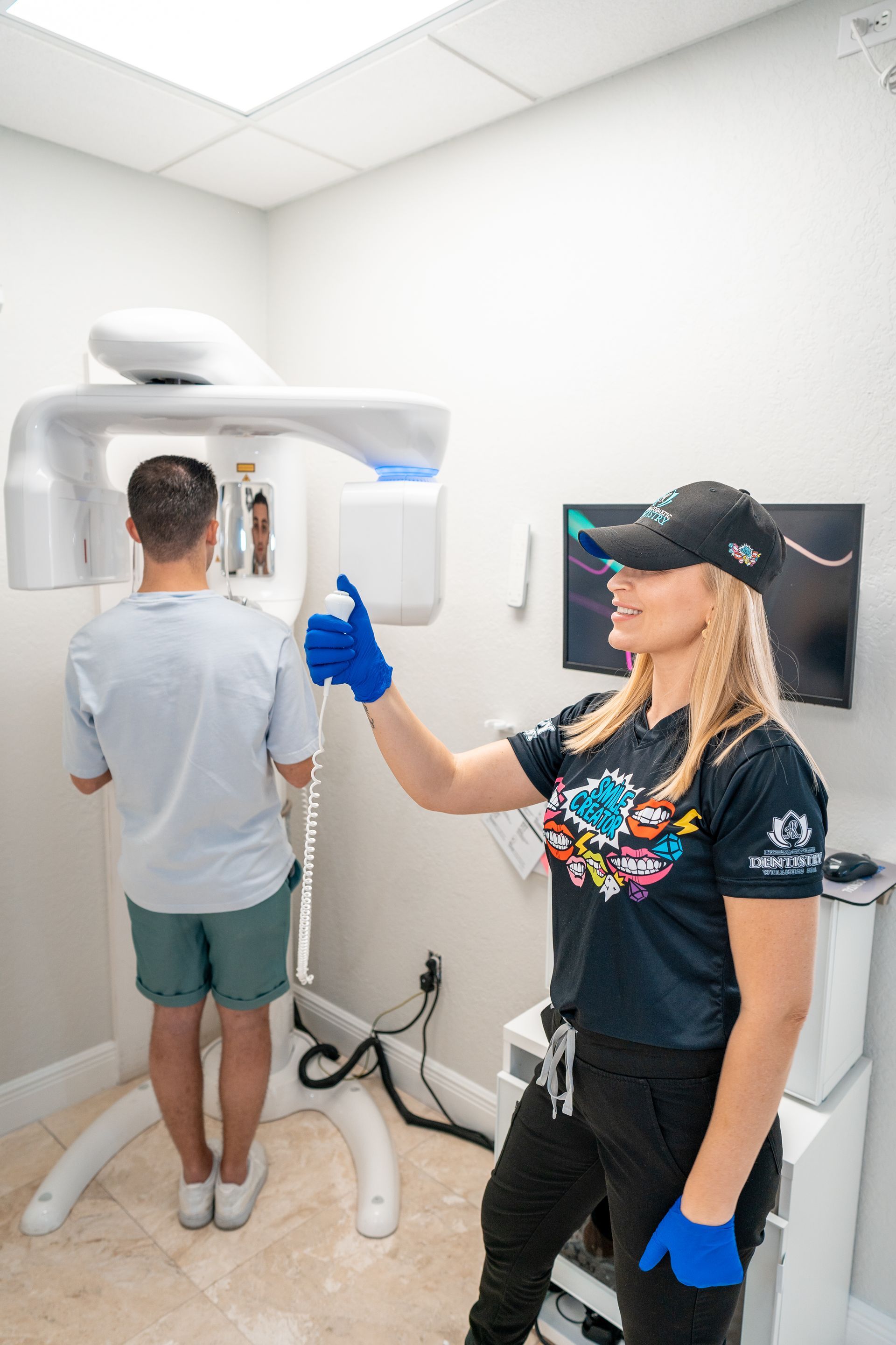 A woman is standing next to a man getting an x-ray of his teeth.