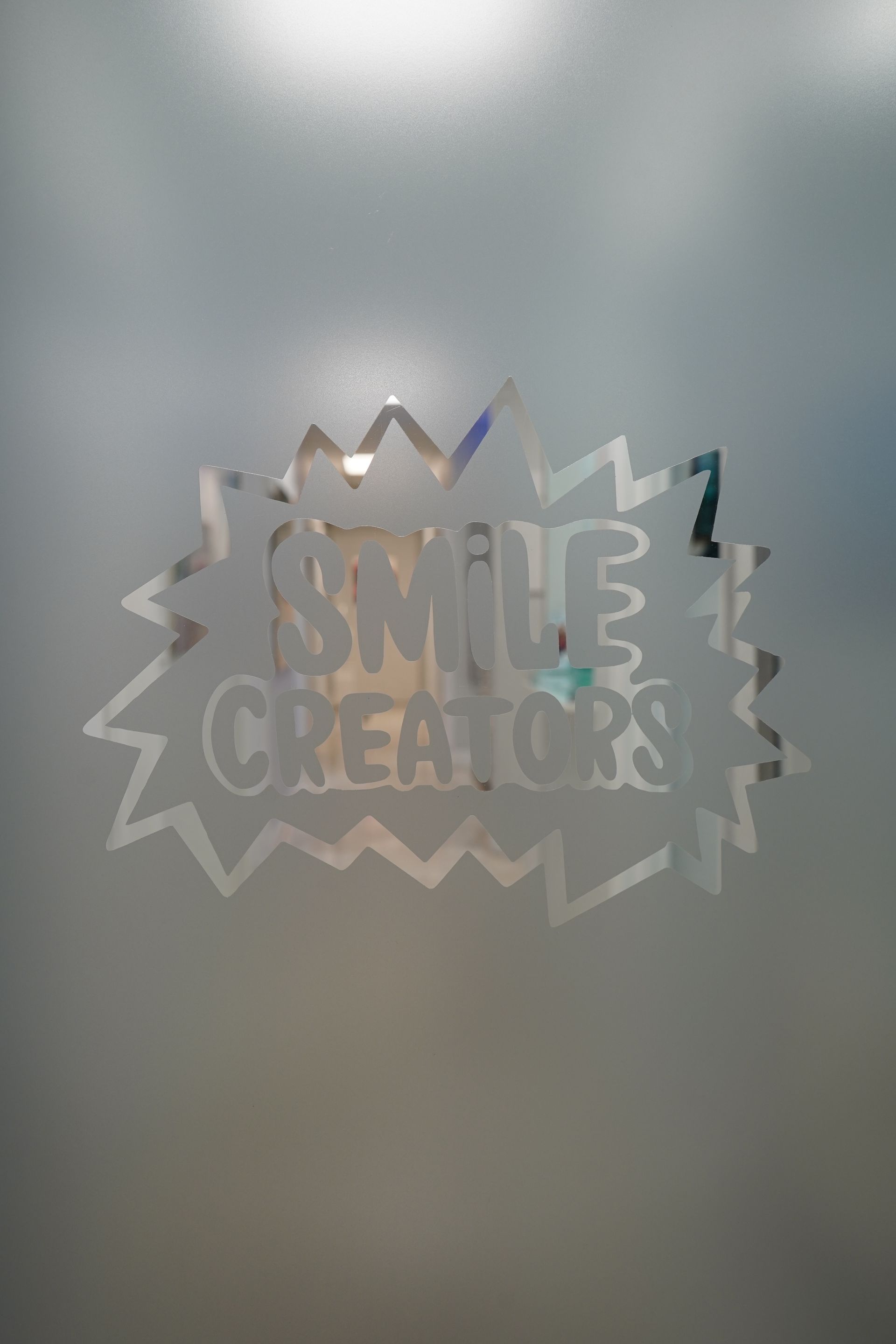 A frosted glass door with the words smile creates written on it