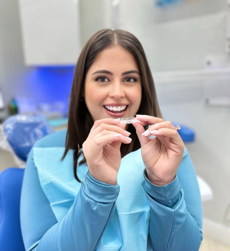 A woman is sitting in a dental chair holding a clear brace.