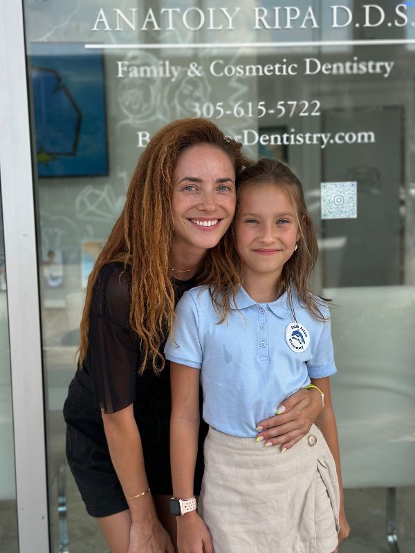 A woman and a little girl are posing for a picture in front of a dentist 's office.
