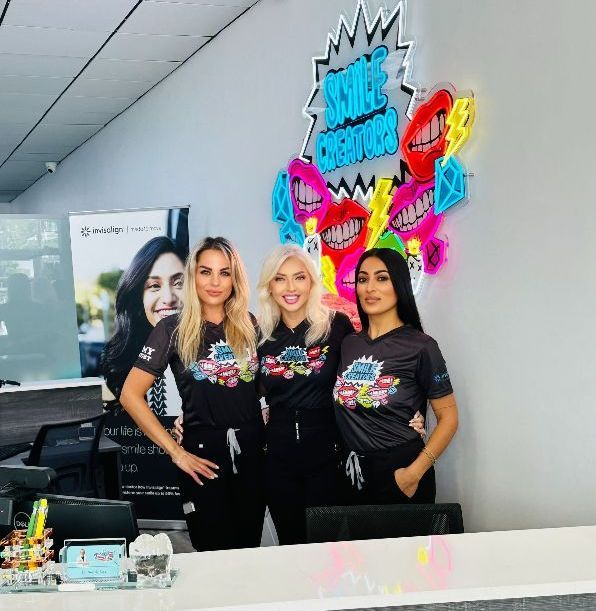 Three women are standing in front of a counter in a dental office.