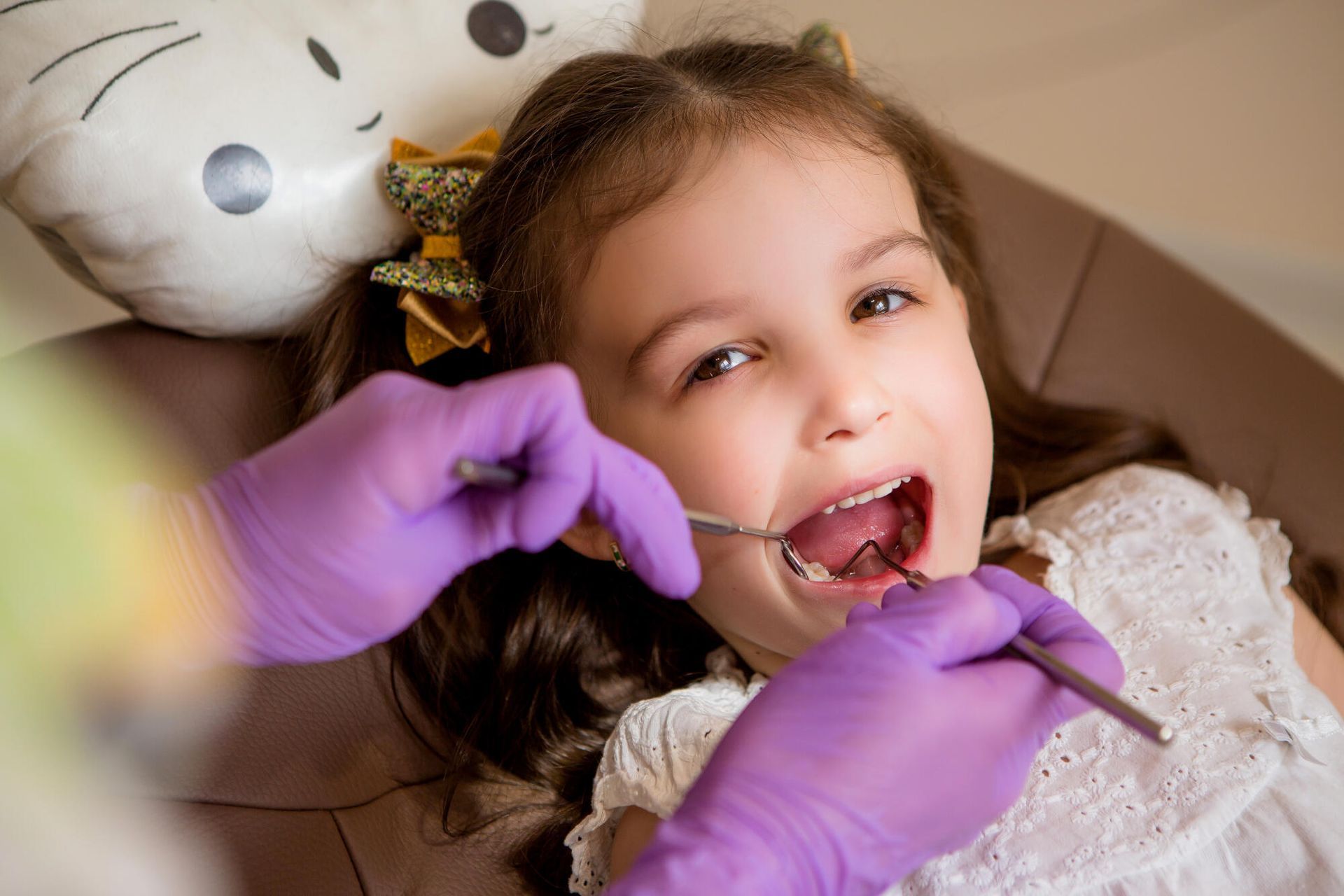 Young child having teeth examined by a dentist with purple gloves, indoors.