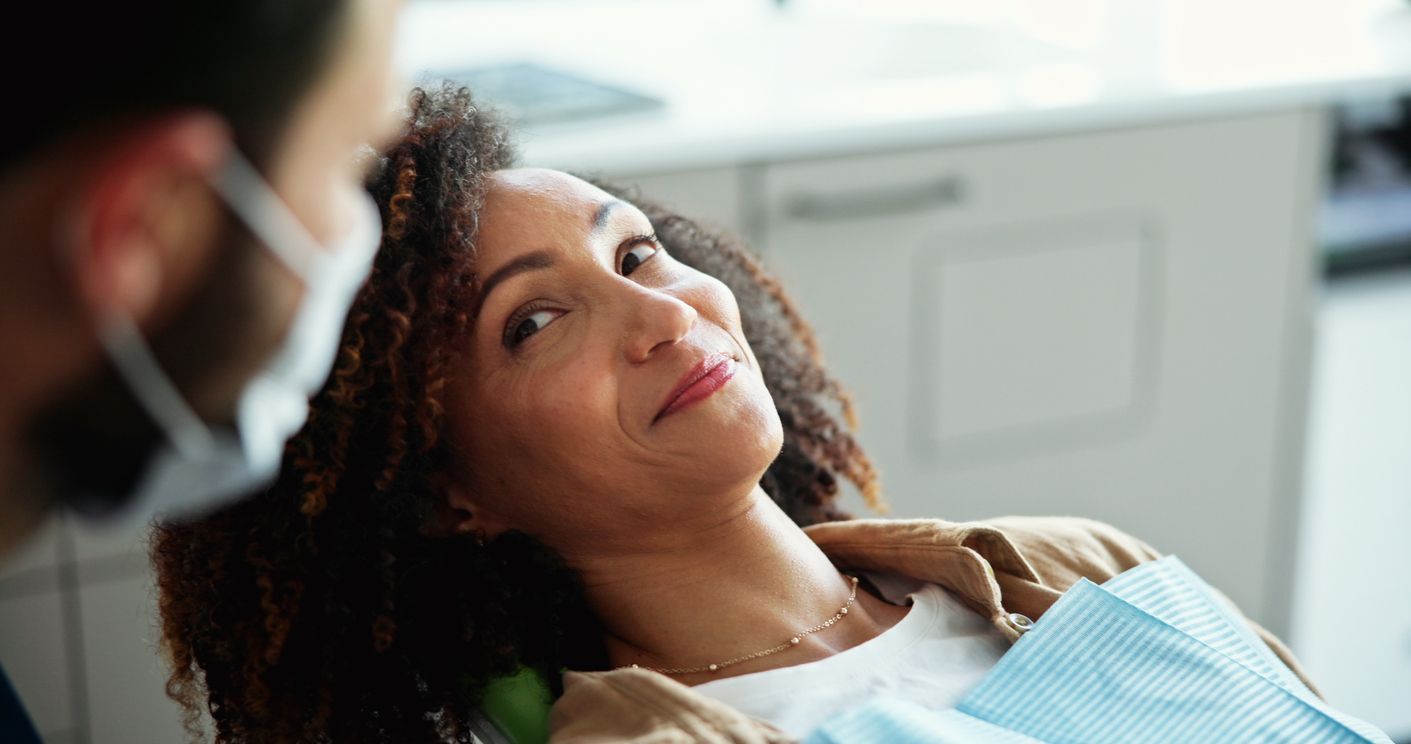 Woman in dental chair looking up at dentist wearing a mask.