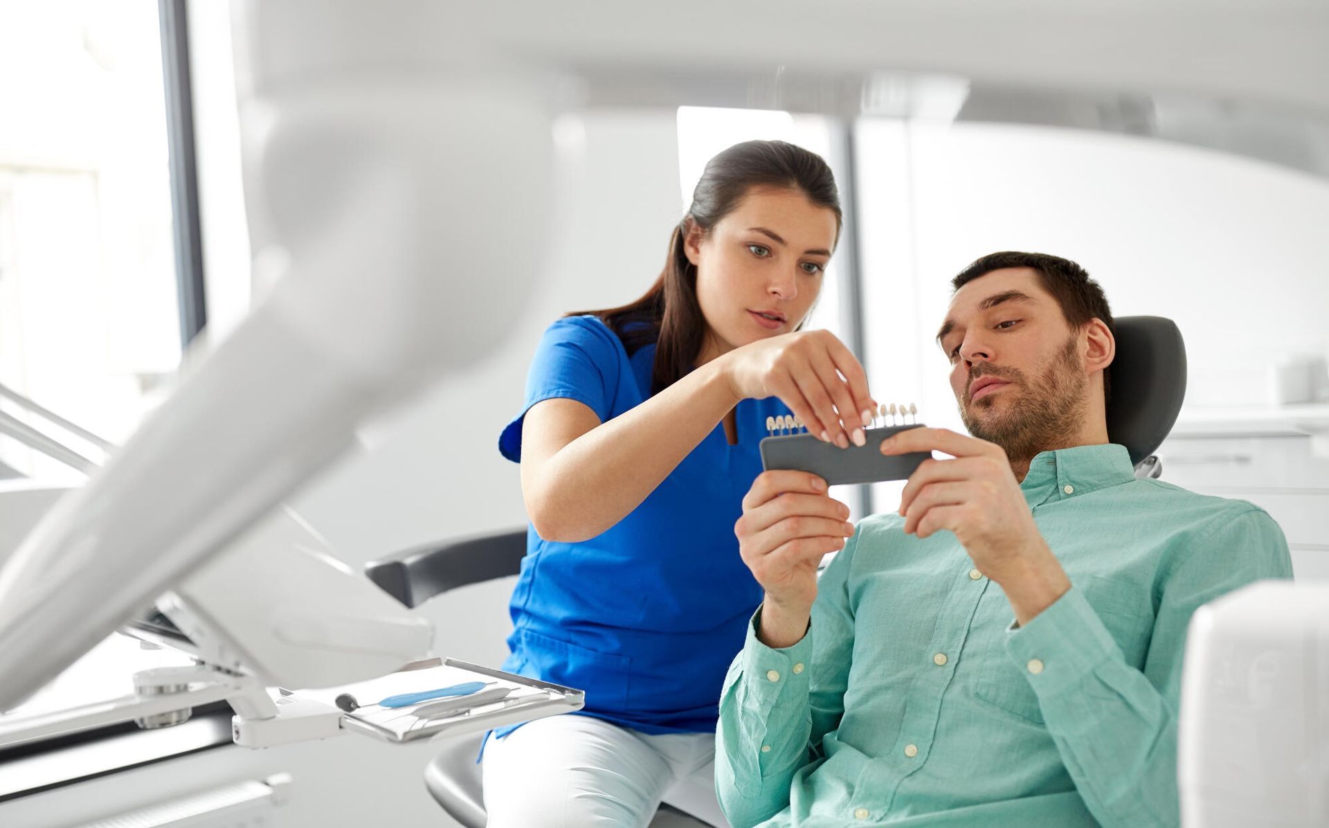 Dentist showing a patient a dental tool in a light-filled office.