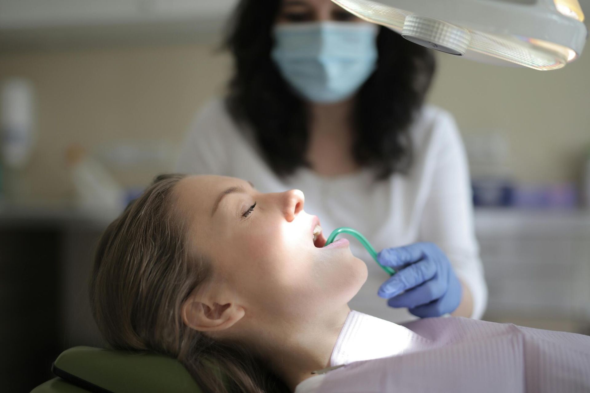 Person receiving dental care, mouth open, dentist with mask and gloves using tools, under bright light.