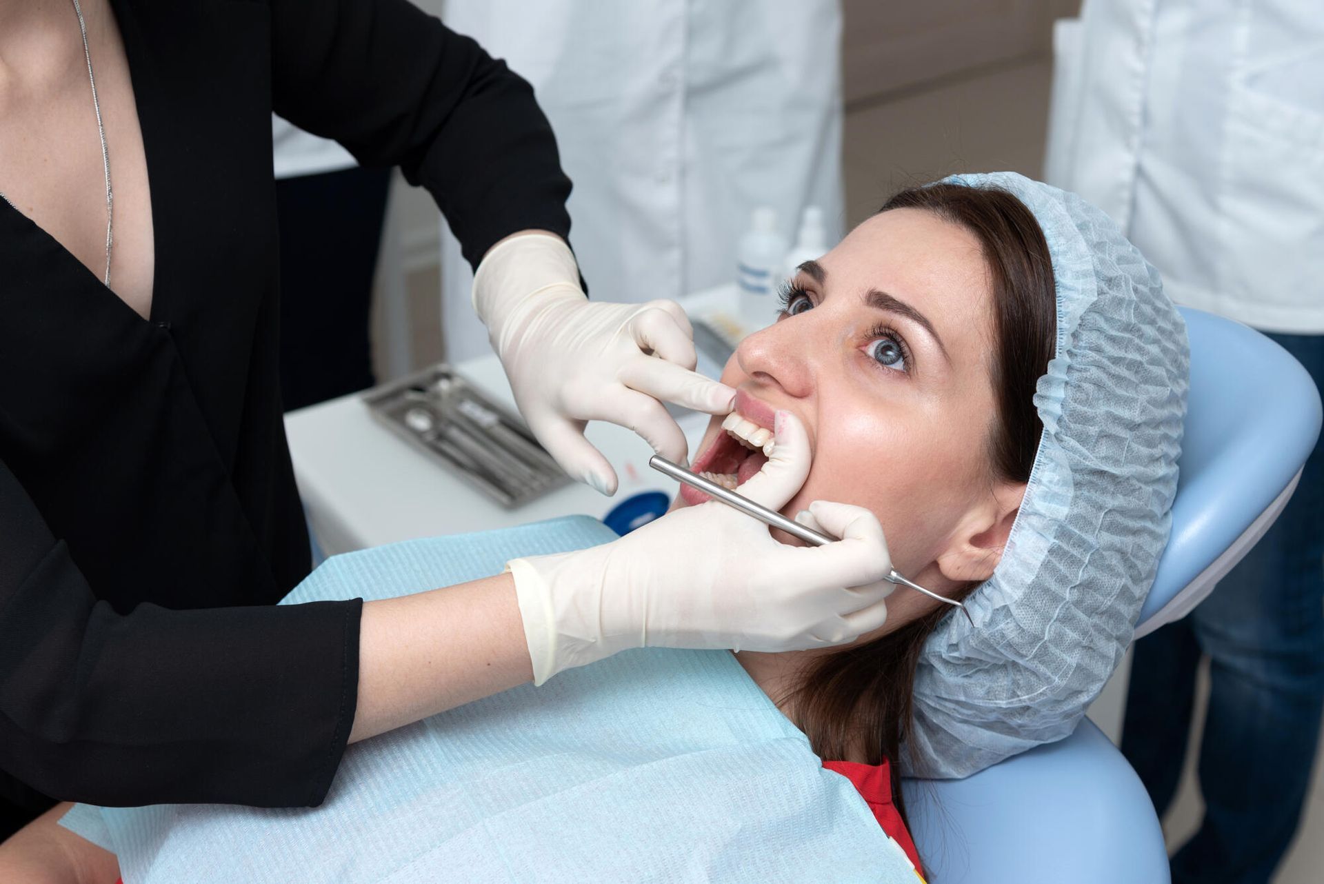 Woman in dental chair with mouth open, dental tools, gloves.