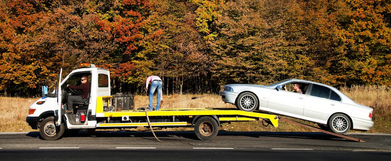 Seattle tow truck driver loading a damaged car onto a flatbed during autumn.
