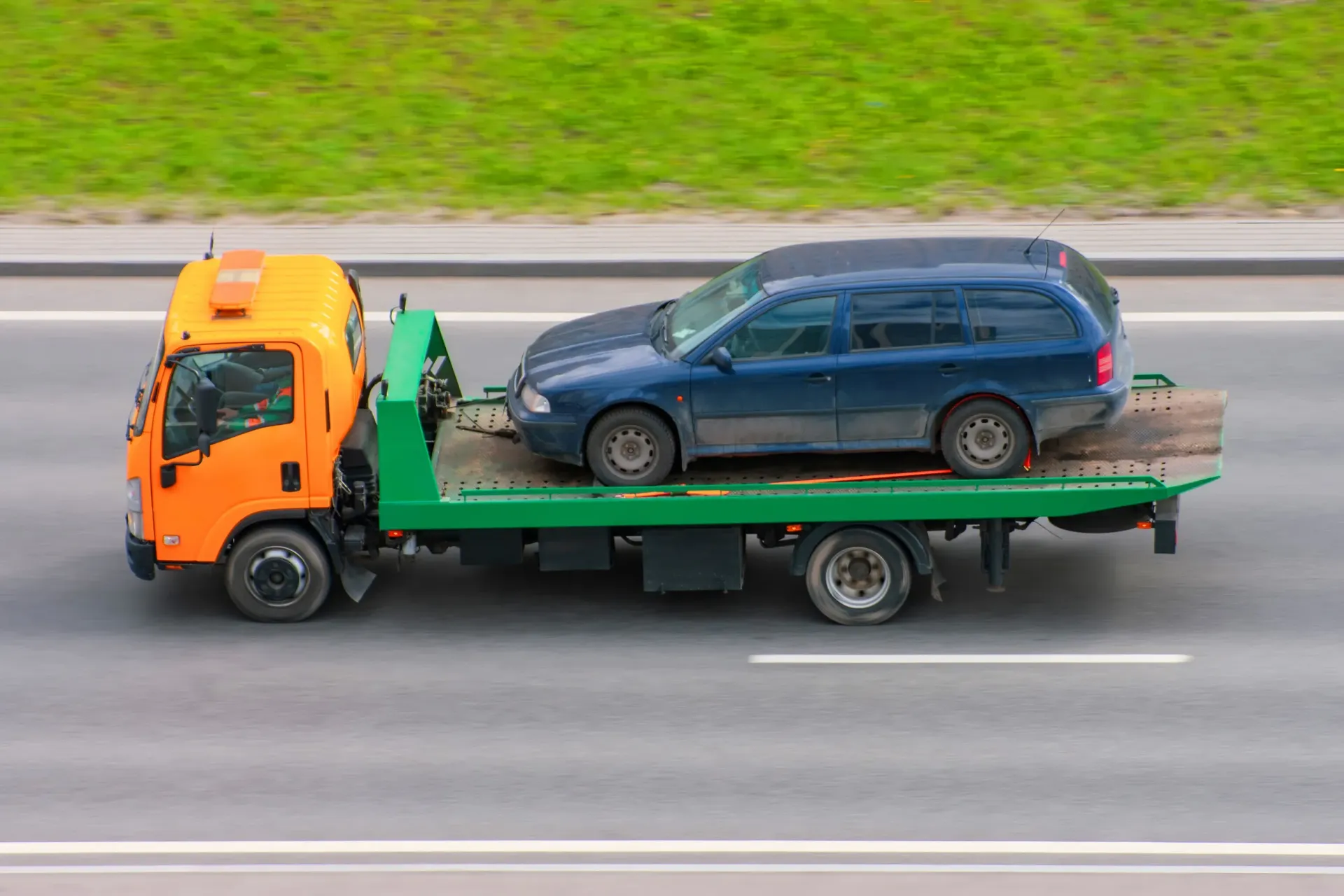 A tow truck is carrying a blue van down the road.