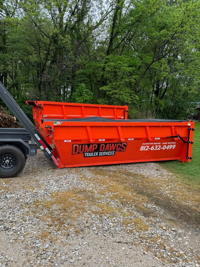 A dumpster is sitting on top of a gravel road next to a truck.