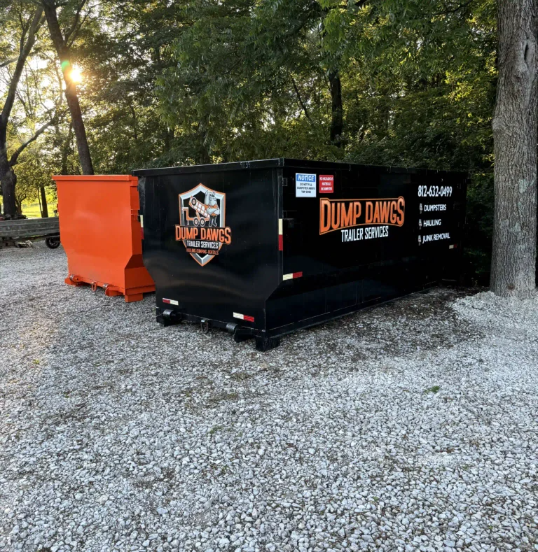 A dumpster is parked in a gravel lot next to an orange dumpster.