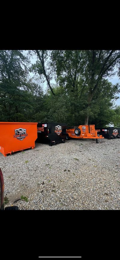 A row of orange dumpsters are parked in a gravel lot.