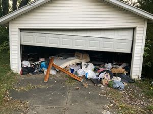 A garage door is open and filled with garbage.