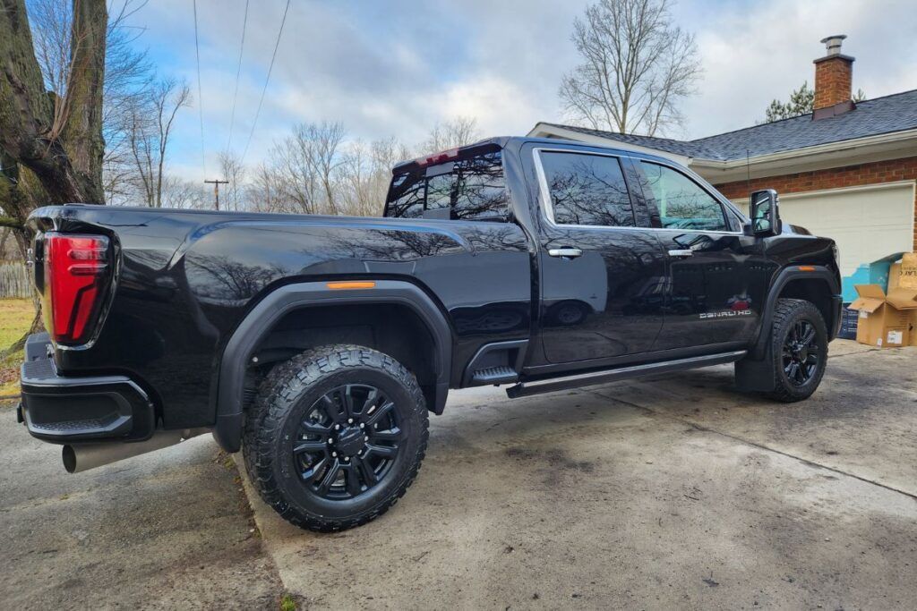 Black GMC truck parked on a driveway with a brick building in the background.