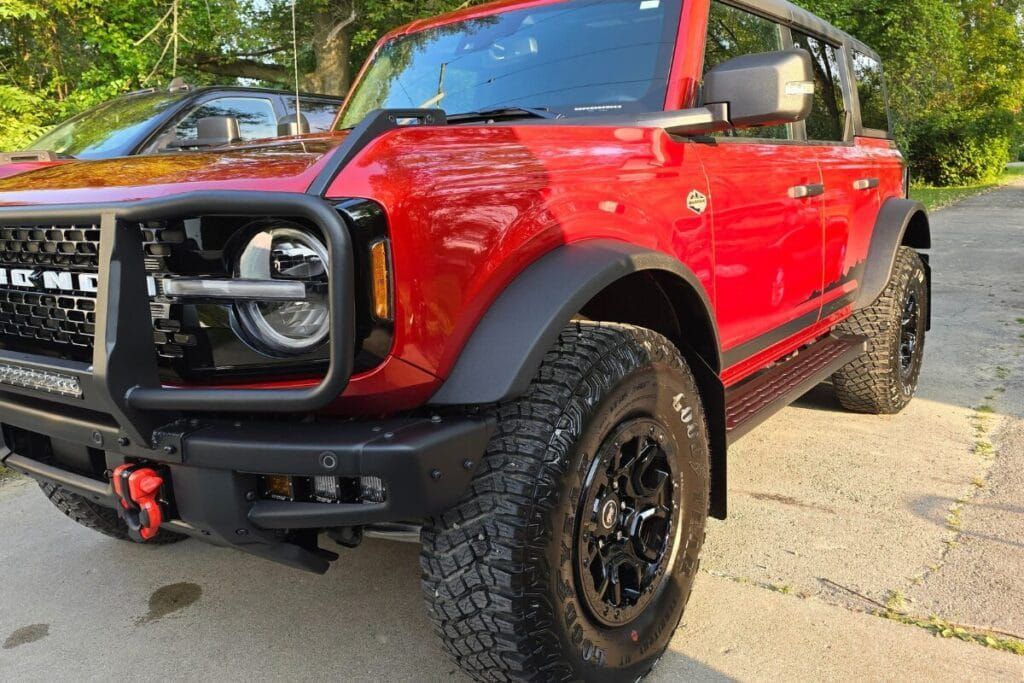 Red Ford Bronco SUV, black accents, rugged tires, outdoor setting.