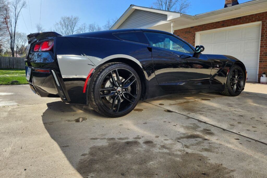 Black sports car parked on a driveway with a garage in the background on a sunny day.