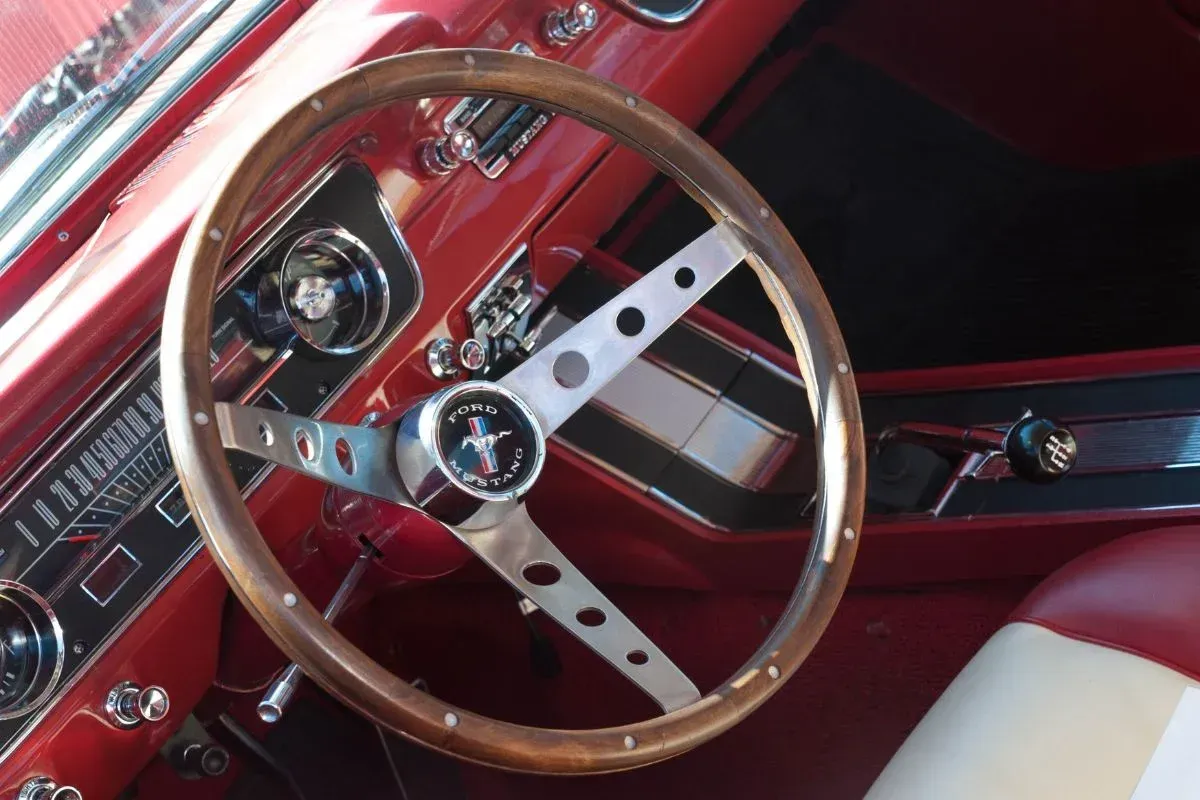 Red classic car interior with wood steering wheel, silver spokes, and Mustang emblem.