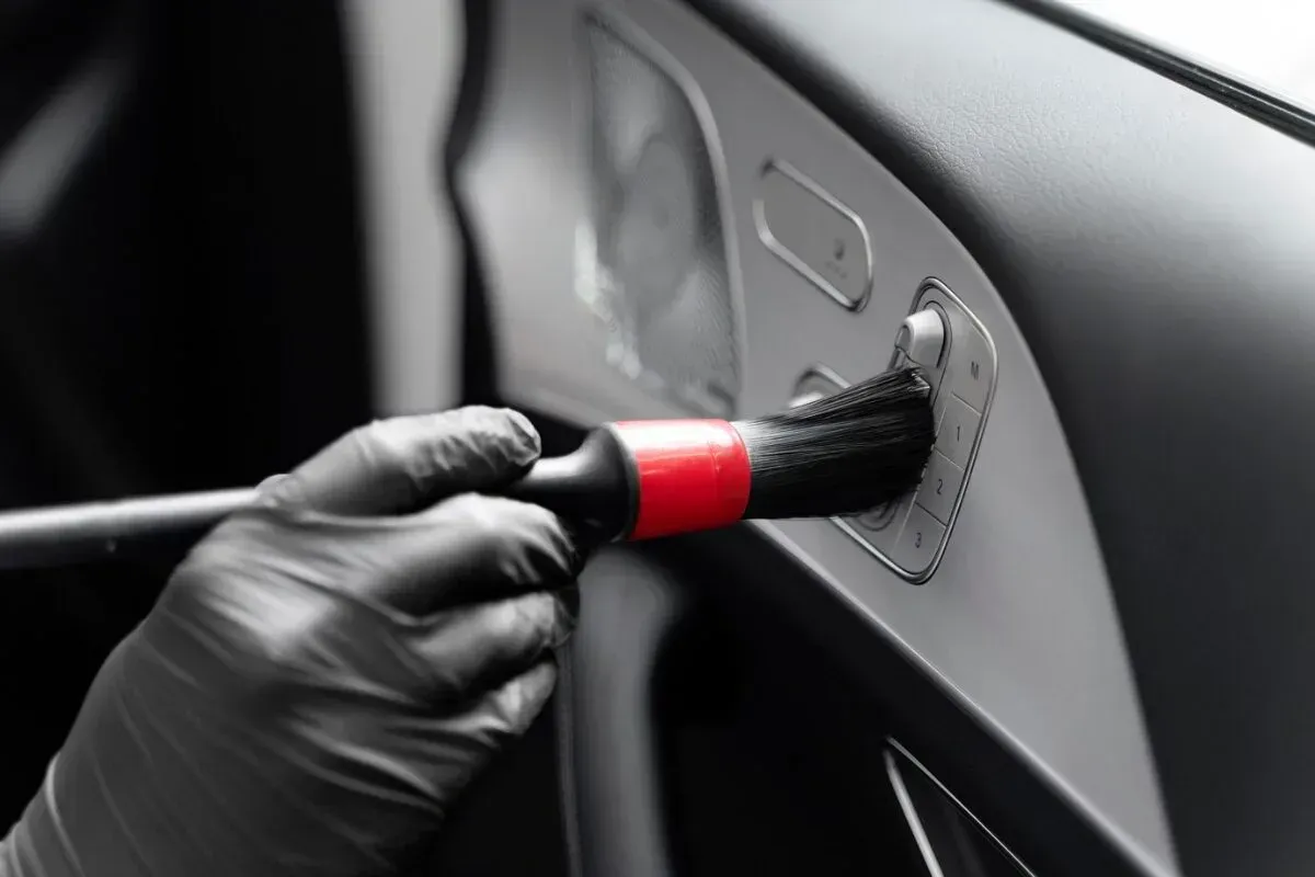 A person wearing black gloves cleaning a car's interior with a soft brush.