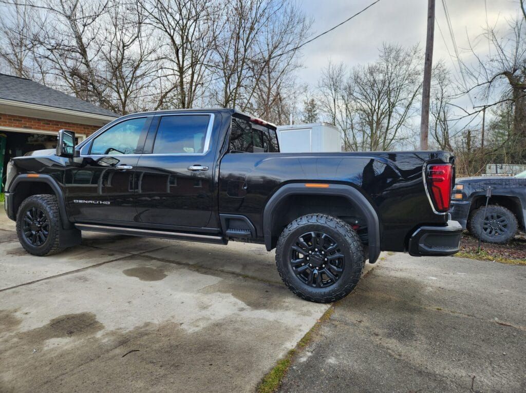 Black GMC truck parked on a concrete surface. Overcast day, trees in the background.