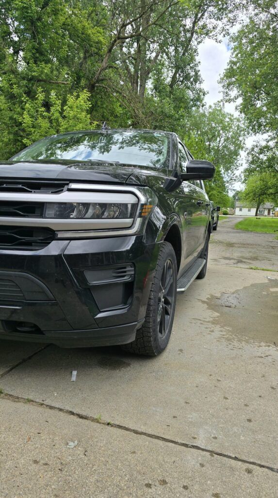 Black SUV parked on a driveway with a street and trees in the background on a cloudy day.