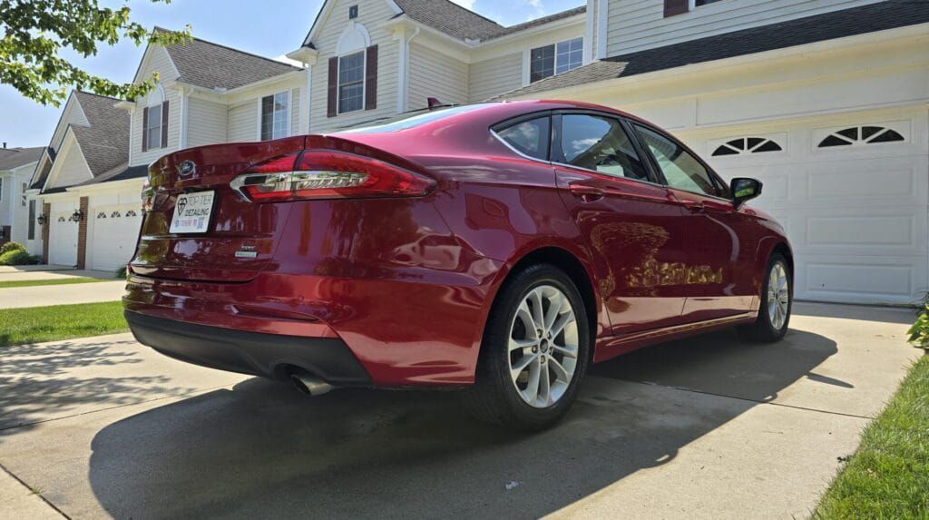Red car parked in front of a two-story house with a two-car garage on a sunny day.