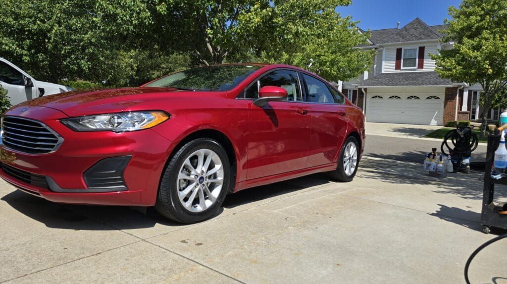 Red Ford sedan parked on a driveway, sunny day. A house with a white garage in the background.