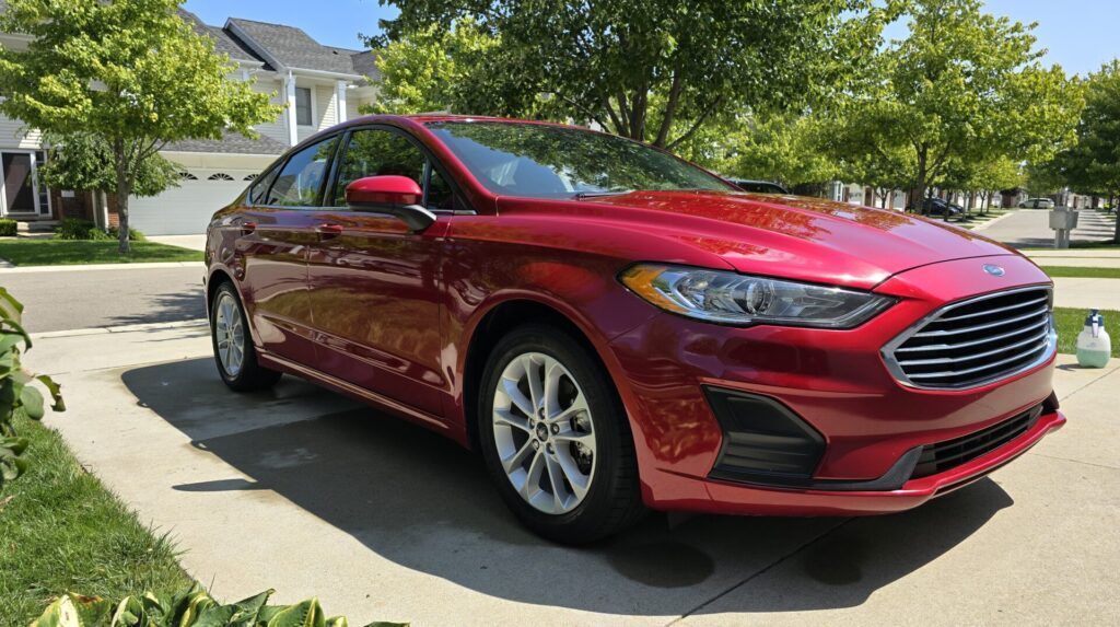 Red Ford Fusion parked on a driveway in front of a house on a sunny day.