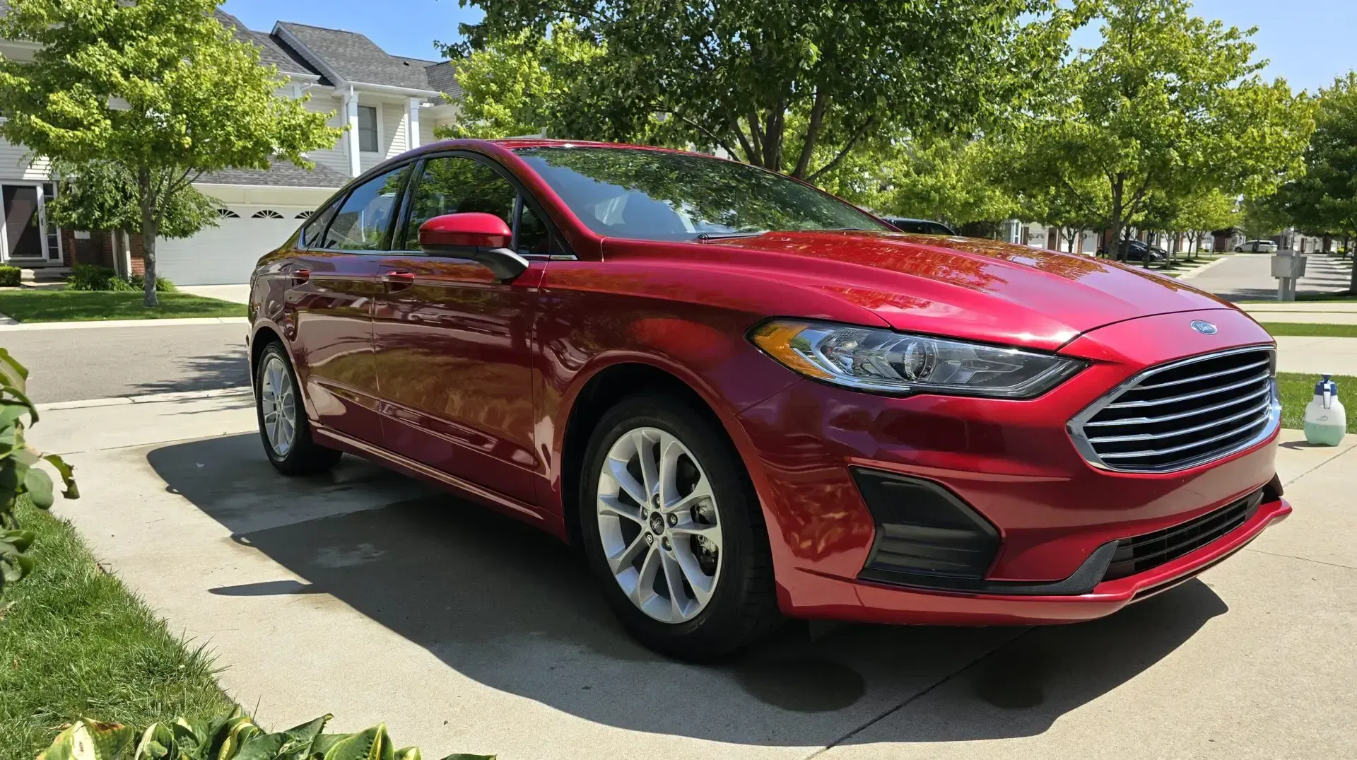 Red Ford Fusion sedan parked on a driveway with green grass and trees in the background.