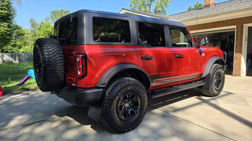 Red Ford Bronco parked in front of a garage with black accents and spare tire on the back.