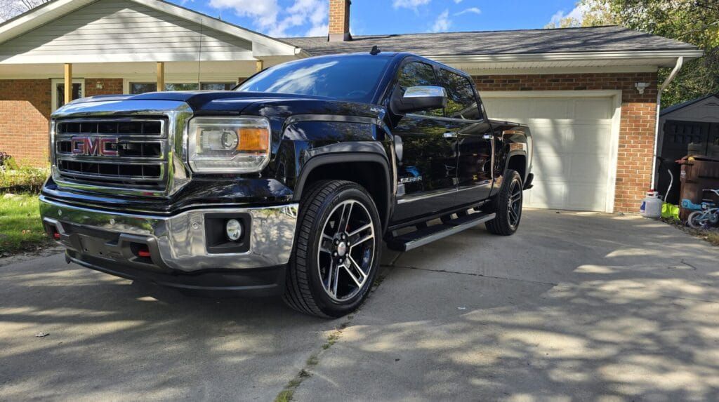 Black GMC Sierra pickup truck parked in front of a house with a garage.