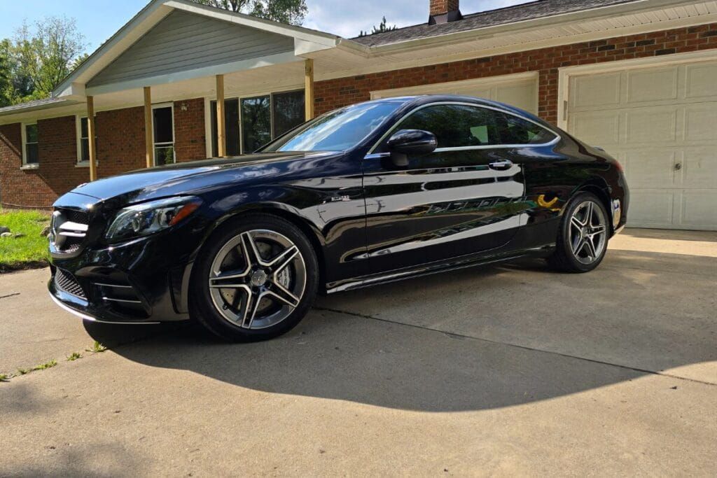 Black Mercedes coupe parked on a driveway in front of a house.
