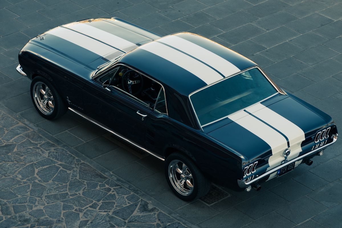 Dark blue classic car with white racing stripes, parked on a stone surface.
