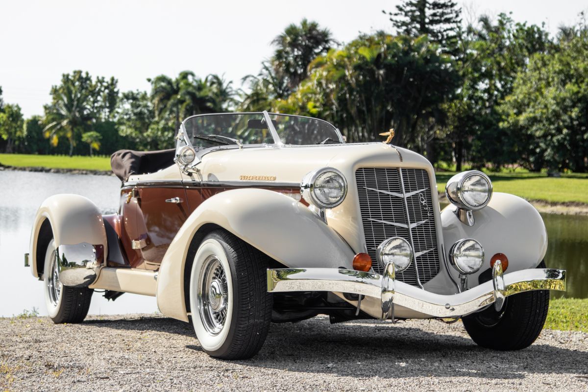 Cream and brown vintage Auburn convertible parked by a lake.