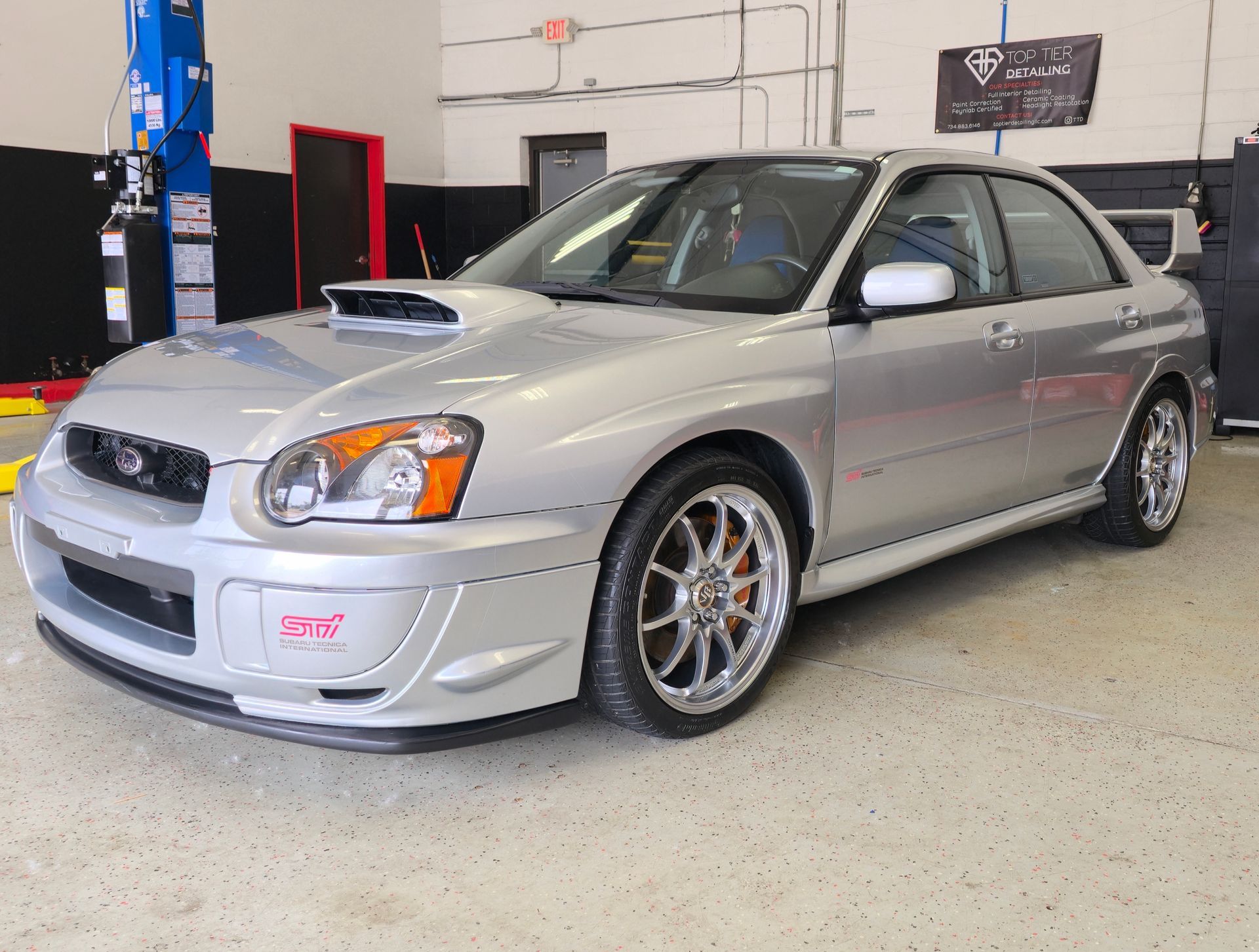 Silver Subaru WRX in a garage, with custom wheels and modifications.