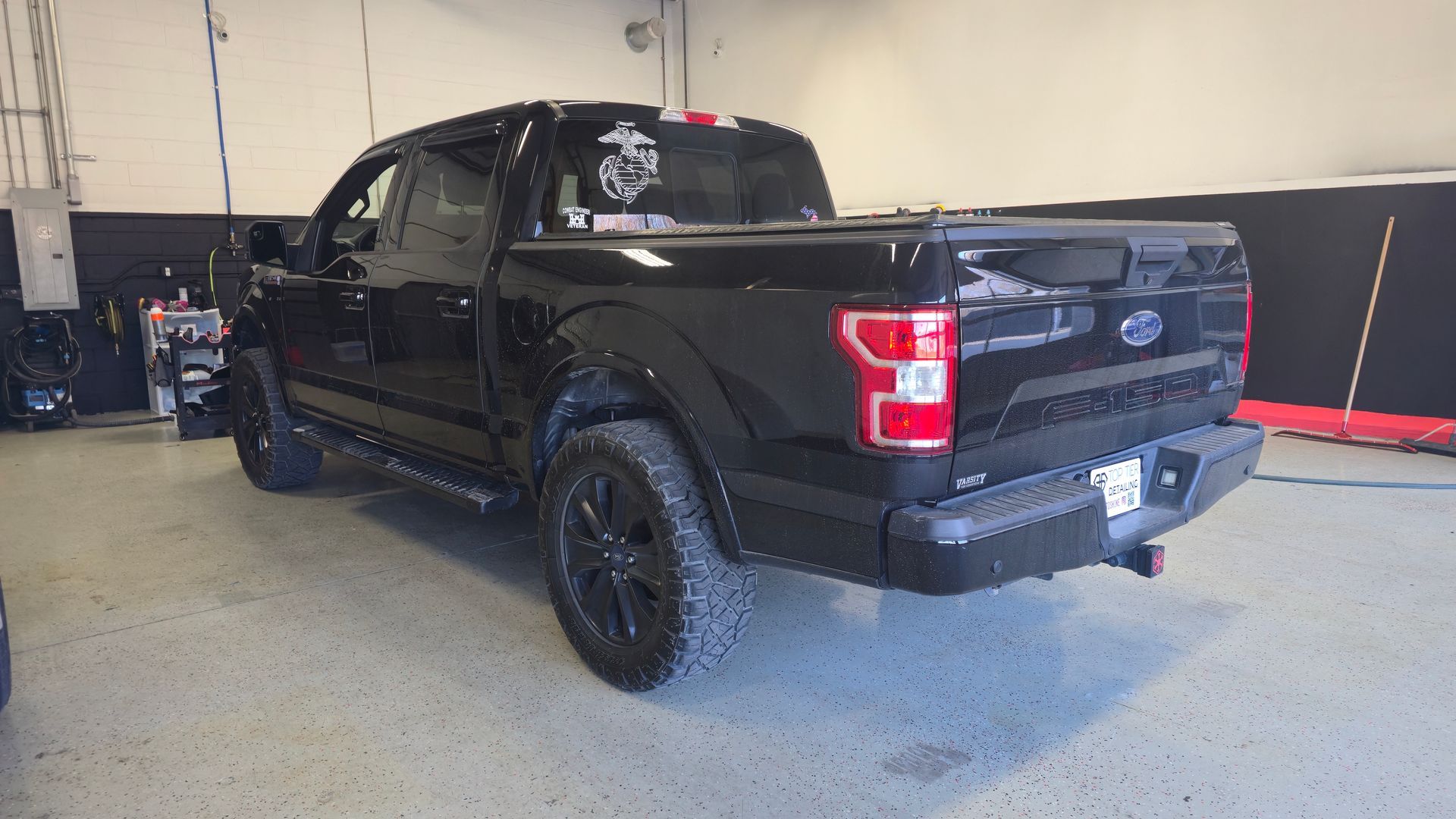 Black Ford F-150 truck parked in a garage. Dark wheels, black body, and black trim.