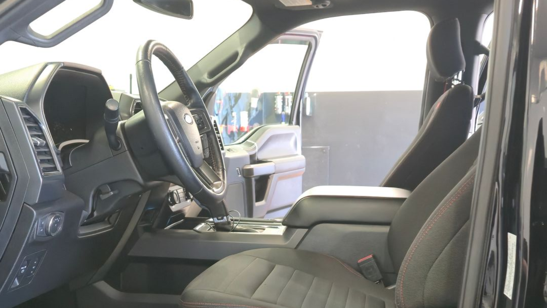 Black vehicle's open cabin, showing driver's seat, steering wheel, and control panel, potentially for a truck or utility vehicle.