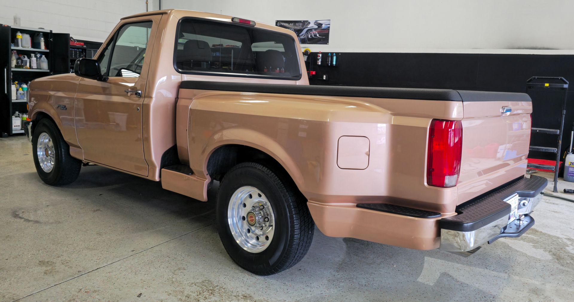 A gold Ford pickup truck parked inside a garage, viewed from a side-rear angle.