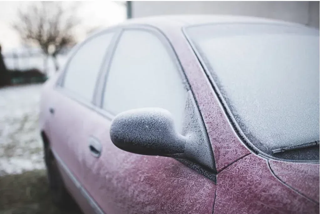 Frost-covered maroon car, side view. Outdoors in a winter setting.