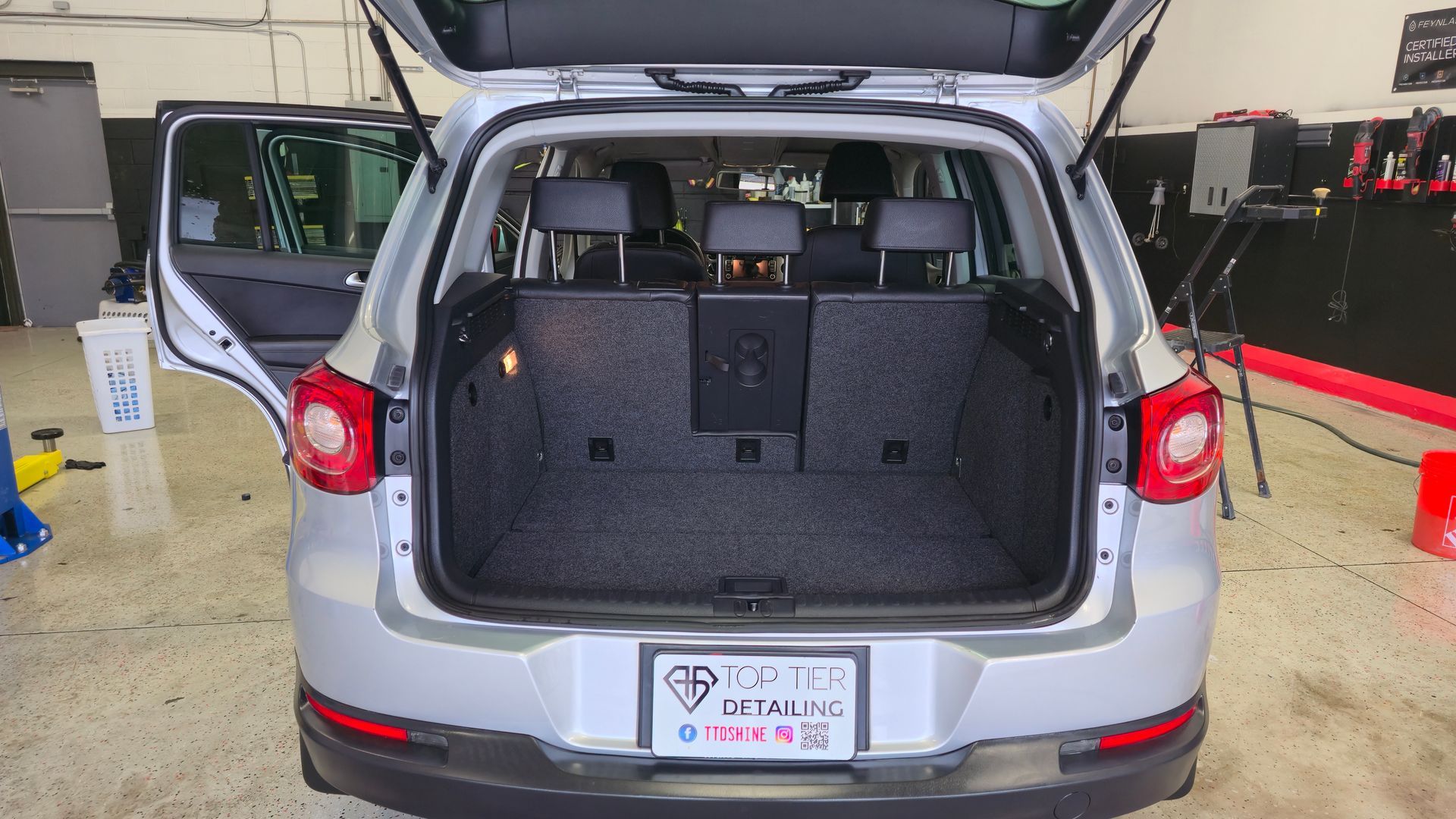 Silver SUV with trunk open, interior visible; back door open, detailing shop in background.